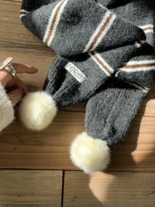 Detailed view of the dark gray knit winter scarf featuring warm pom pom and chic stripes.