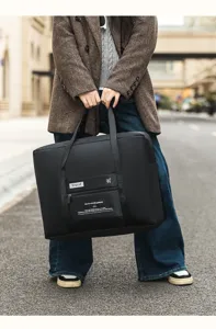 Vue détaillée du sac de voyage pliable noir avec poche avant zippée et poignées robustes.