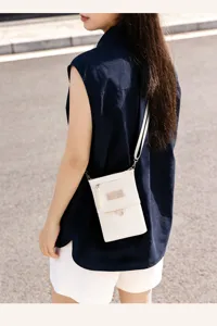Outdoor detail view of the white crossbody passport holder bag worn by the model, compact style.