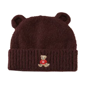 Brown knit bear ear beanie hat detail view, cute embroidered patch and thick warm winter fabric.