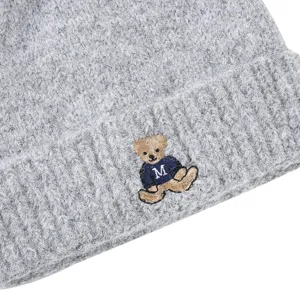 Close-up detail of grey knit beanie hat featuring cute embroidered bear motif with letter M.