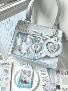 Detail view of the light blue ita bag featuring a clear window, bow, and anime character badges.