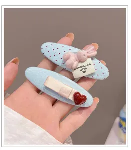 Detail shot of cute Korean blue polka dot fabric hair clips with fluffy bunny and red heart decor.