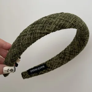Detail view of dark green woven tweed headband, showing fine texture and inner label.