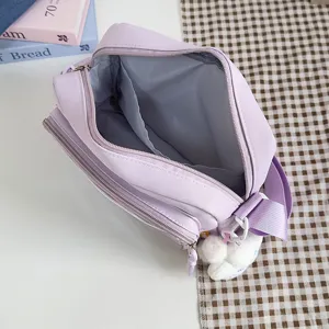 Detail view of a trendy purple canvas crossbody ita bag with cute plush doll pendant.