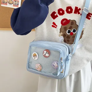 Light blue canvas crossbody ita bag with clear mesh pocket for enamel pins and badges display.