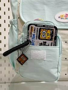 Detailed close-up of light green canvas backpack pocket with cute cartoon card and pendant.