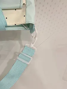 Close-up detail showing the light blue strap, white plastic buckle, and polka dot canvas.