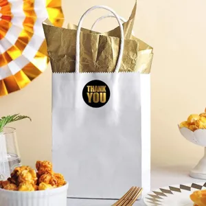 Close-up detail of white paper gift bag with gold tissue paper and thank you sticker.