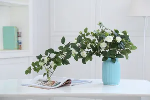 Detail view of artificial white rose vine arrangement in a blue ribbed vase on a clean table.