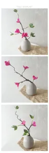 Detail shot of artificial bougainvillea branch with green leaves in textured grey ceramic vase.