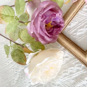 Close up of artificial silk roses bouquet with vintage wooden frame and white fabric background.