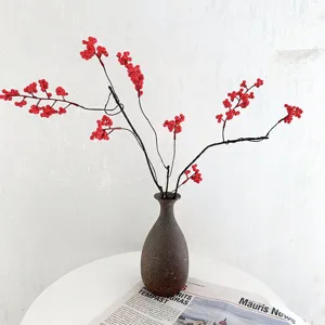 Vista detallada de rama de bayas rojas artificiales en jarrón marrón, decoración Zen.