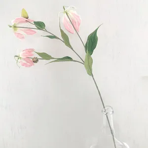 Close-up detail view of artificial pink gloriosa lily flower branch inside clear glass vase