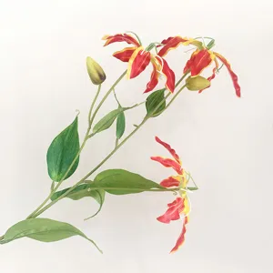 Detailed view of artificial gloriosa lily branch with realistic red yellow wavy petals and green leaves.