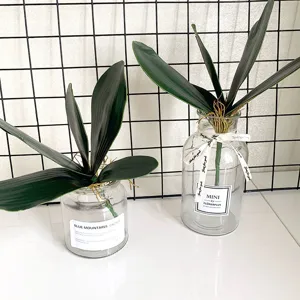 Artificial orchid leaves detail shot, faux foliage and glass vase for flower arrangement decor.