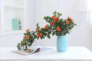 Detailed view of artificial orange rose vine in a light blue vase for home decor setup.