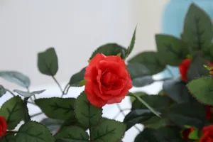 Close-up detail of artificial red silk rose flower with green leaves for home decor.