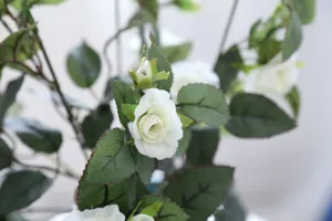 Close-up detail of artificial white rose flower and green leaves for home decoration.