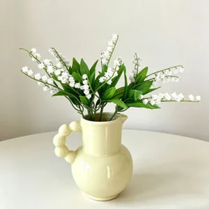 Artificial lily of the valley bouquet with yellow ceramic vase, elegant home decor detail.