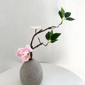 Artificial floral branch detail, gray ceramic vase with pink flowers and green leaves.