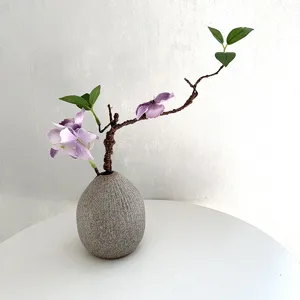Close-up of decorative artificial floral arrangement with twisted branch and grey vase.