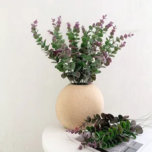 Ramo de plantas artificiales de eucalipto verde en jarrón redondo de cerámica decorativo.