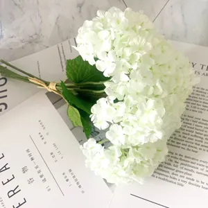 Detailed shot of white artificial hydrangea flower bouquet with green leaves, elegant home decor.