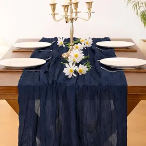Detailed view of dark blue cheesecloth table runner styled on a wooden table with candles.
