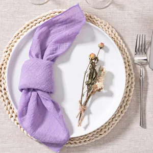 Close-up view of a purple wrinkled fabric napkin styled on a white plate with dry flower.