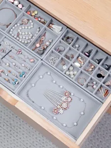 Detalle de bandeja de joyería de terciopelo gris, organizador multi-compartimento para anillos.