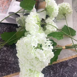 Artificial white hydrangea flower bouquet with green leaves for wedding decor and photography detail.