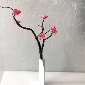 Artificial pink peach blossom flower branch in white ceramic vase for home decor detail.