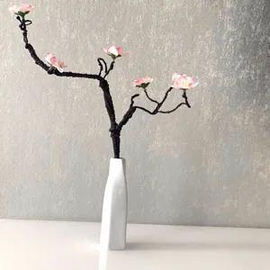 Close-up detail of artificial peach blossom branch in white ceramic vase for decor.