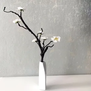 Close-up detail of artificial plum blossom branch in a white ceramic vase, home decor.