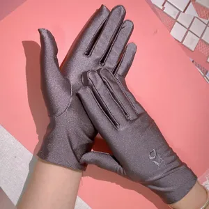 Dettaglio in primo piano di guanti da sole elasticizzati in raso da donna con ricamo.