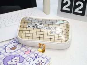 Close-up detail of white transparent pencil pouch with cute grid design and gold dual zippers.