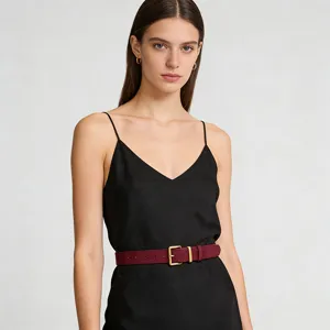 Detail view of a stylish women suede belt with gold buckle worn over a chic black dress.