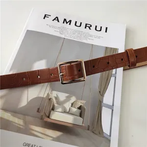 Close up view of the brown crocodile pattern leather belt with a polished gold square buckle.