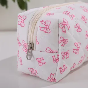 Detailed view of white quilted cosmetic pouch with pink bow pattern and smooth zipper.