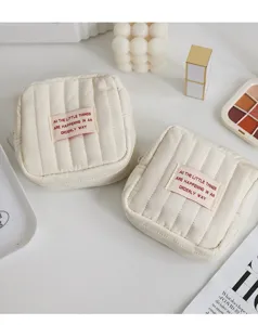 Detail view of mini quilted makeup pouch, cute beige storage bag with slogan patch and zipper.