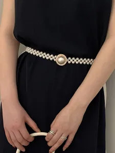 Detail shot of elastic pearl waist belt with decorative metal round buckle for dress styling.