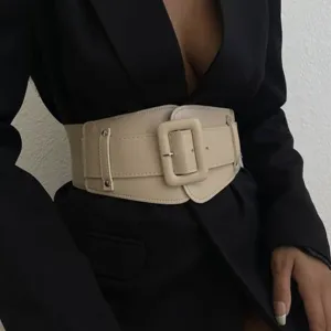 Detail view of the wide beige elastic waist belt with large square buckle worn on black blazer.