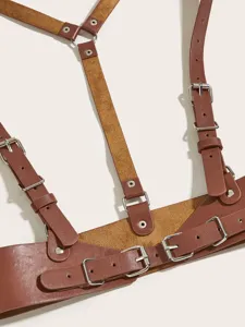 Dettaglio imbracatura in pelle marrone con fibbie metalliche regolabili e cintura punk.