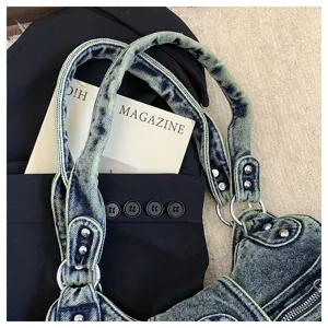 Close-up detail of vintage washed denim shoulder bag with metal rings and rivets hardware.