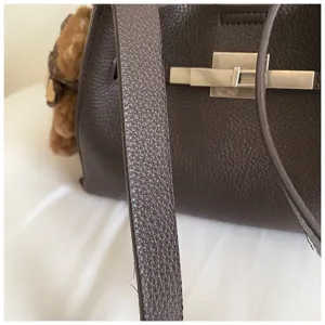 Detailed shot of dark brown leather shoulder bag with metallic lock hardware and plush charm.