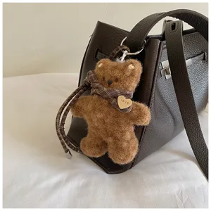 Plush bear keychain with plaid scarf hanging on a chic dark brown leather shoulder bag.