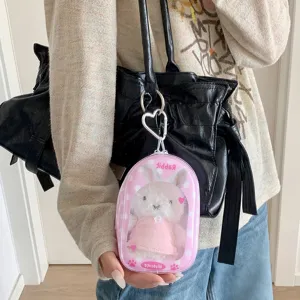 Vue détaillée du sac de présentation de poupée capsule transparente avec lapin en peluche.