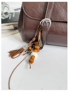 Close-up detail of dark brown leather shoulder bag with chic wooden bead tassel pendant.