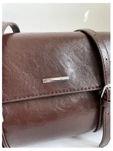 Brown leather shoulder bag detail showing textured surface and metallic bar decoration.